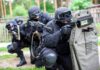 Tactical team with shields and rifles in formation.