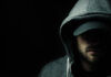 Man in dark hoodie and cap, face partially shadowed.