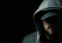 Man in dark hoodie and cap, face partially shadowed.