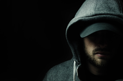 Man in dark hoodie and cap, face partially shadowed.