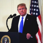 Donald Trump speaking at a podium with American flag.