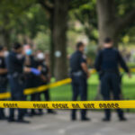 Police officers behind yellow crime scene tape in park.