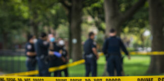 Police officers behind yellow crime scene tape in park.