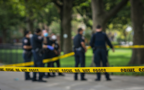 Police officers behind yellow crime scene tape in park.