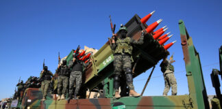 Armed soldiers on a truck with mounted missiles.