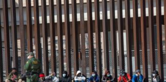 Border patrol agent with group of seated immigrants.