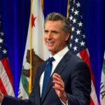 Man speaking at podium with American and California flags.