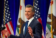 Man speaking at podium with American and California flags.