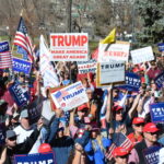 Crowd holding Trump signs and American flags at rally.