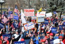 Crowd holding Trump signs and American flags at rally.