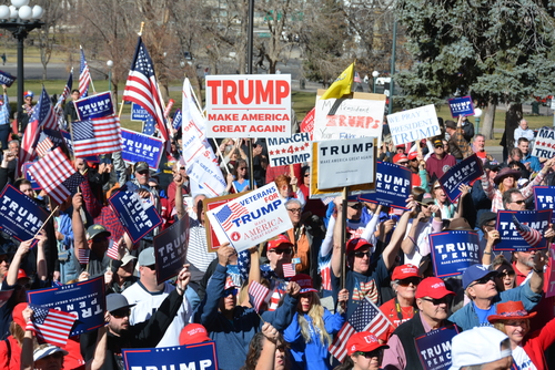 Crowd holding Trump signs and American flags at rally.