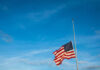 American flag at half-mast against a blue sky.