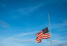 American flag at half-mast against a blue sky.