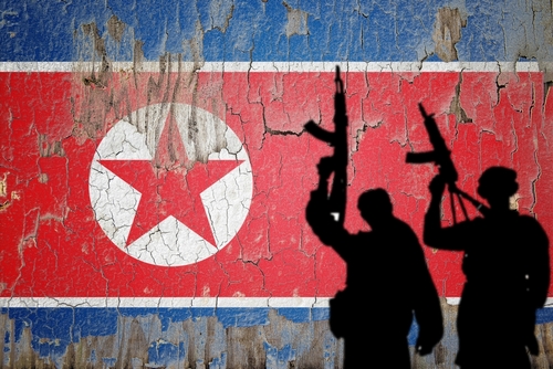 Silhouetted soldiers in front of North Korean flag.