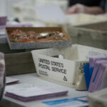 USPS worker handling mail-in ballots at a sorting facility.