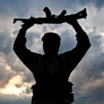 Silhouette of a person holding a rifle against a cloudy sky