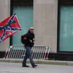 Virginia STRIPS Confederate Tax Breaks After 76 Years… Man walking with Confederate flag on city sidewalk.