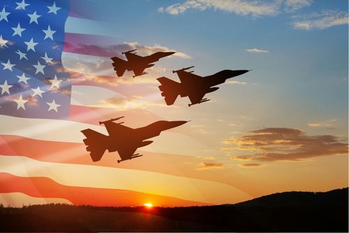shutterstock_2259886557 Three fighter jets fly in formation at sunset with a translucent U.S. flag overlay