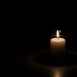 A lit candle in a glass holder against a dark background
