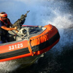 Person on orange boat holding machine gun.
