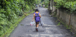 A child walking down a rural path carrying school supplies
