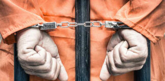 Handcuffed person in orange jumpsuit behind bars.