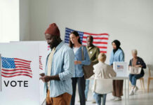 Feds Raid Voter Rolls — What’s Next? People voting in a polling station with American flags.