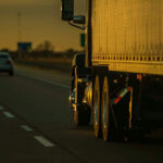 Deadly Crash Sparks English Test Uproar Truck and car driving on highway at sunset.