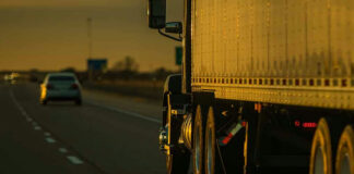 Truck and car driving on highway at sunset.