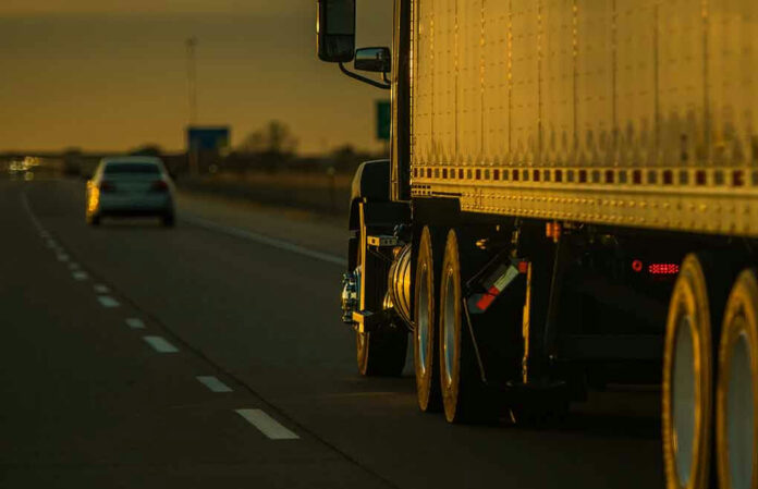 Truck and car driving on highway at sunset.