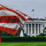 American flag waves before the White House on a cloudy day