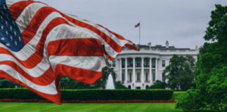 American flag waves before the White House on a cloudy day
