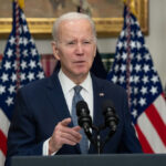 Man speaking at podium with American flags behind