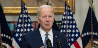 Man speaking at podium with American flags behind