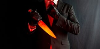 A man in a suit holding a glowing knife against a dark background