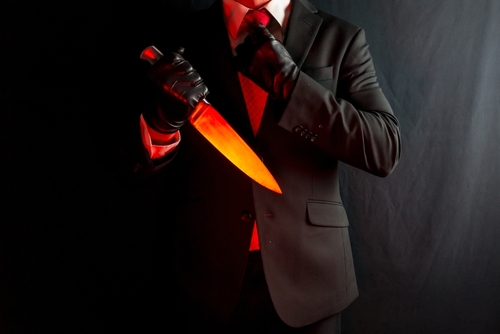 Businessman,In,Dark,Suit,And,Red,Tie,Holding,Sharp,Knife A man in a suit holding a glowing knife against a dark background