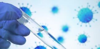 A gloved hand holding a test tube with a clear liquid against a blue virus background