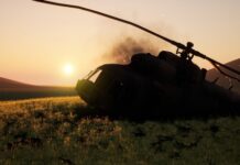 Abandoned military helicopter in a grassy field during sunset