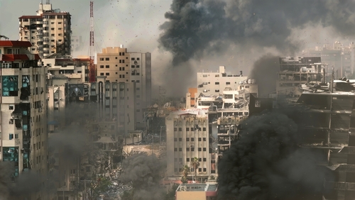 A cityscape showing damaged buildings and thick smoke rising from the ground