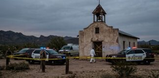 Police vehicles and officers at a crime scene near an abandoned building in a desert area