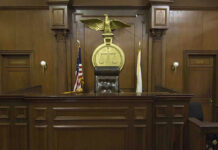 Judges bench in an empty courtroom, scales emblem above.