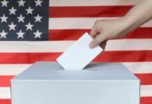 Hand casting ballot into box before U.S. flag