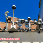 Array of security cameras mounted above a building facade under a clear blue sky