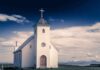 White countryside church with steeple and cross under a dramatic sky