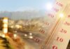 Close-up of a thermometer in hot sun over a blurred road and mountains