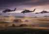 Military helicopters fly low over a rural farm at sunset