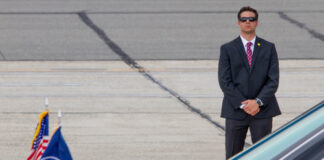 A security guard in a suit stands near a presidential vehicle at an airport